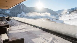 Un balcón cubierto de nieve con mobiliario exterior, con vistas a un paisaje montañoso y un complejo de esquí al fondo.