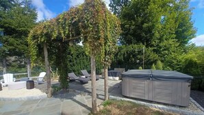 A backyard with a hot tub, lounge chairs, and a pergola covered with vines.