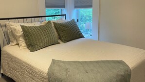 A bedroom with a bed, two windows with blinds, and an air conditioning unit.