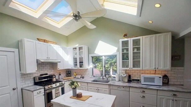 A kitchen with white cabinets, a central island, a ceiling fan, and a skylight.