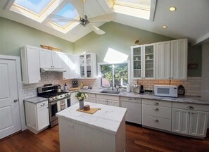 A kitchen with white cabinets, a central island, a ceiling fan, and a skylight.