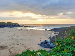 Ein Strand mit einer felsigen Klippe und einem Sonnenuntergang im Hintergrund.