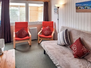 Ein gemütliches Zimmer mit zwei roten Stühlen, einem grauen Sofa, einem Heizkörper und einer Lampe.