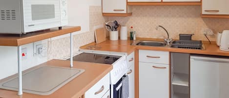 A compact kitchen with a microwave, stove, sink, and a small refrigerator.