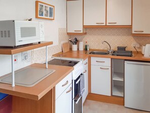 Eine kleine Küche mit Mikrowelle, Herd, Spüle und kleinem Kühlschrank.
