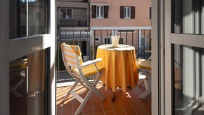 En balkon med et bord og to stole, fliset gulv og en bygning i baggrunden.