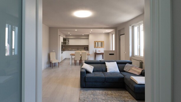 En moderne stue med en mørkeblå hjørnesofa, en lille måtte og et spiseområde med bord og stole.