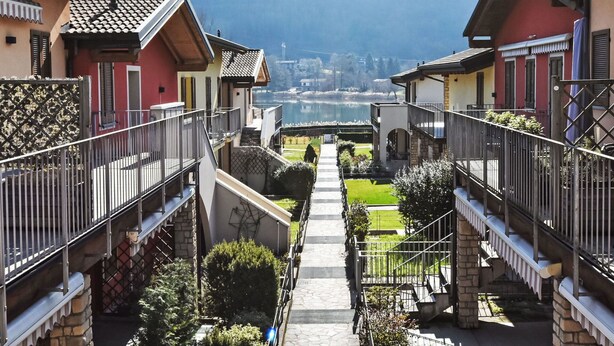 Zona residencial con un camino central que lleva a un lago, rodeada de casas con balcones y muros de piedra.
