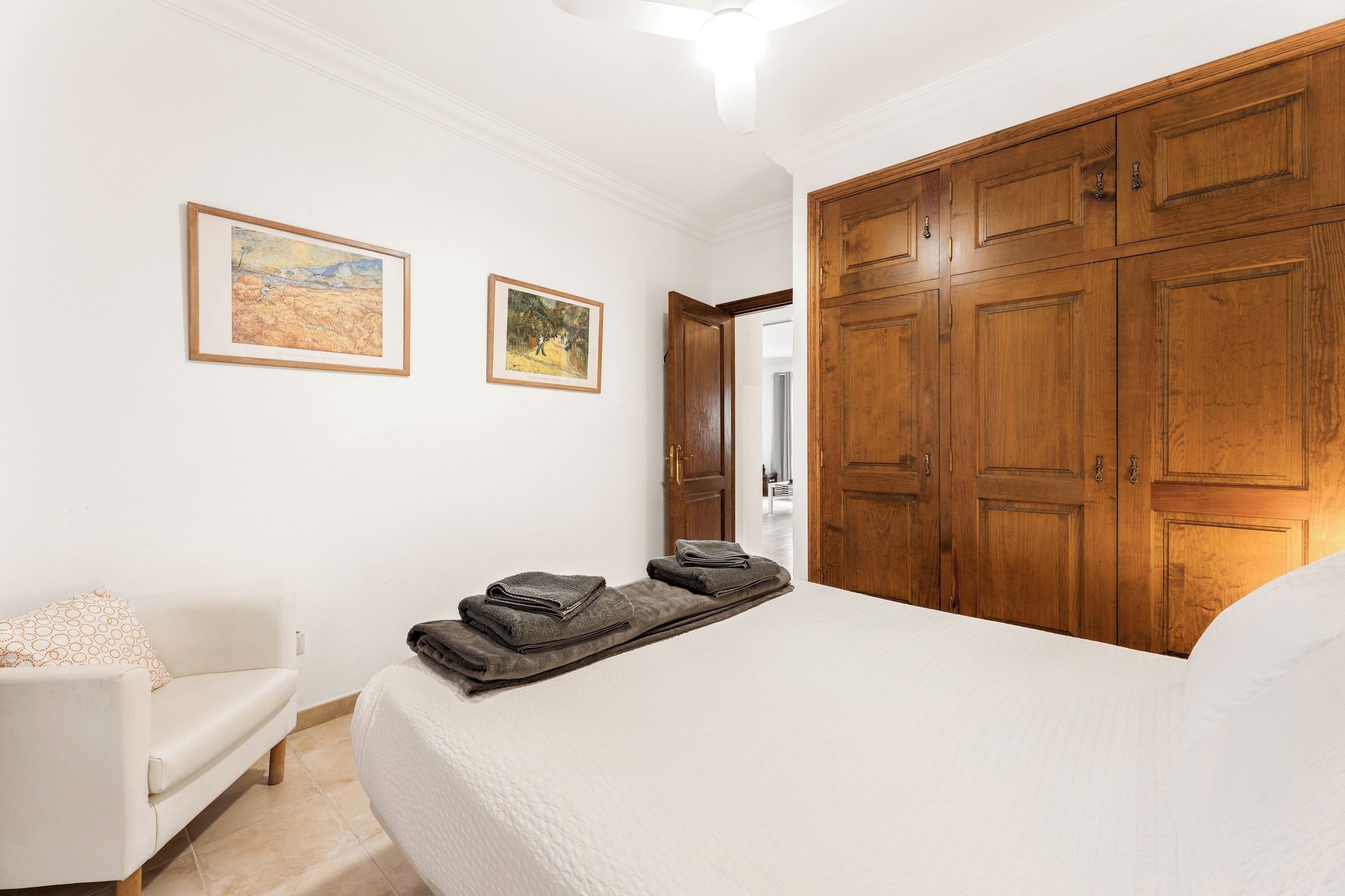 Een slaapkamer met een bed, een houten garderobe, een witte bank en twee prenten in lijsten aan de muur.
