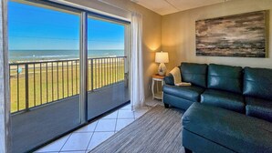 A living room with a view of the beach, a sofa, a lamp, and a painting on the wall. -  Spacious Ormond Oceanfront  3 bedroom Condo (Ormond Beach)