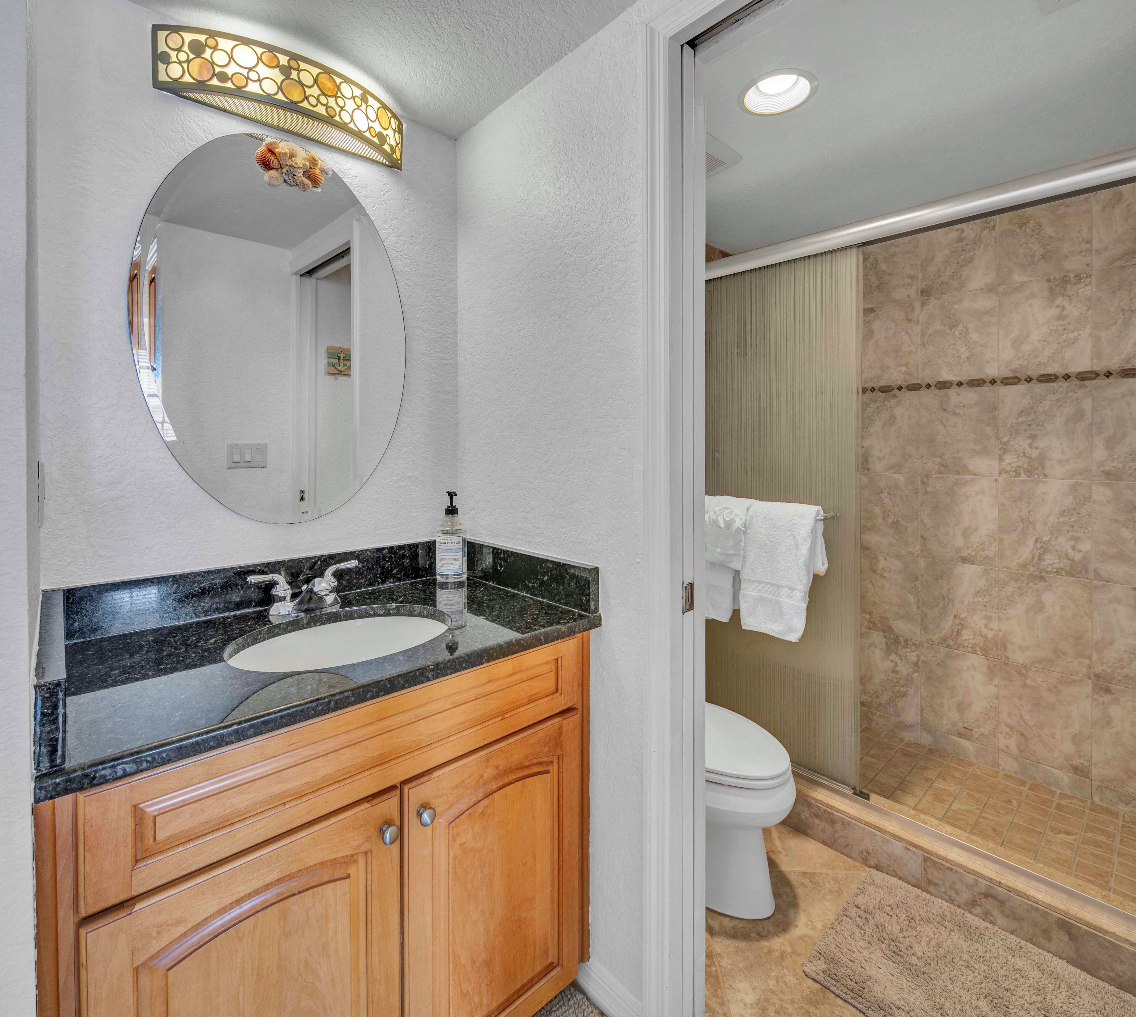 A bathroom with a round mirror, a sink, wooden cabinets, and a shower area.