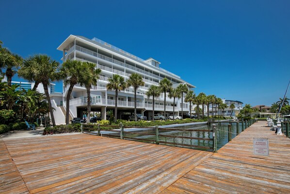 A waterfront hotel with a wooden deck, palm trees, and a clear blue sky.