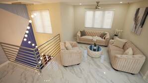 A spacious living area with a beige sofa set, a coffee table, and a staircase with a railing. - Luxury 6BR Villa w/ Pool, Rooftop Deck & lower level Lounge/ 2 Car garage/AC (Oistins)