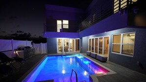 A swimming pool with a built-in slide, a covered patio area, and a dining space visible through glass doors. - Luxury 6BR Villa w/ Pool, Rooftop Deck & lower level Lounge/ 2 Car garage/AC (Oistins)
