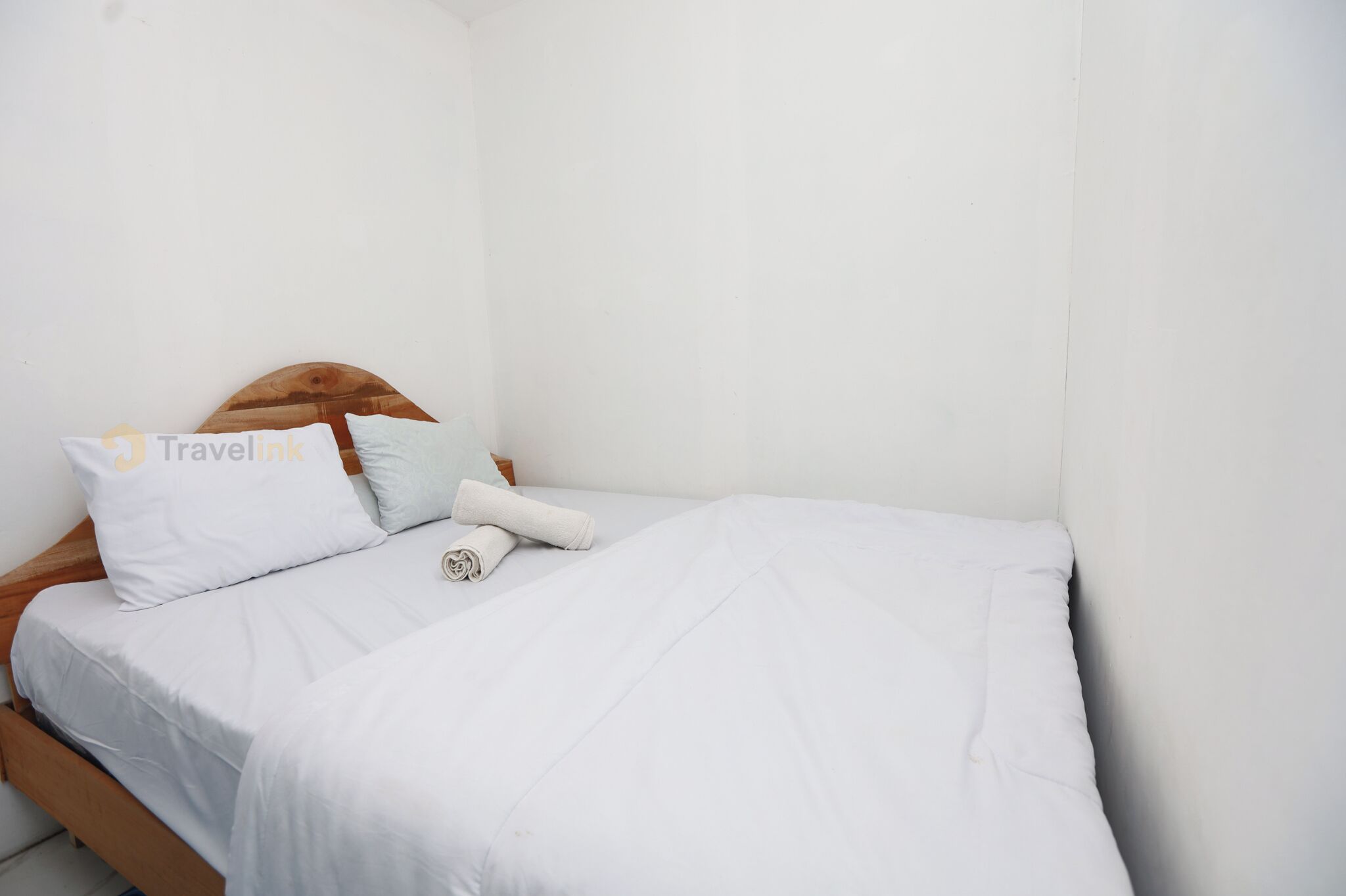 A small, neatly made bed with white bedding and a wooden headboard.