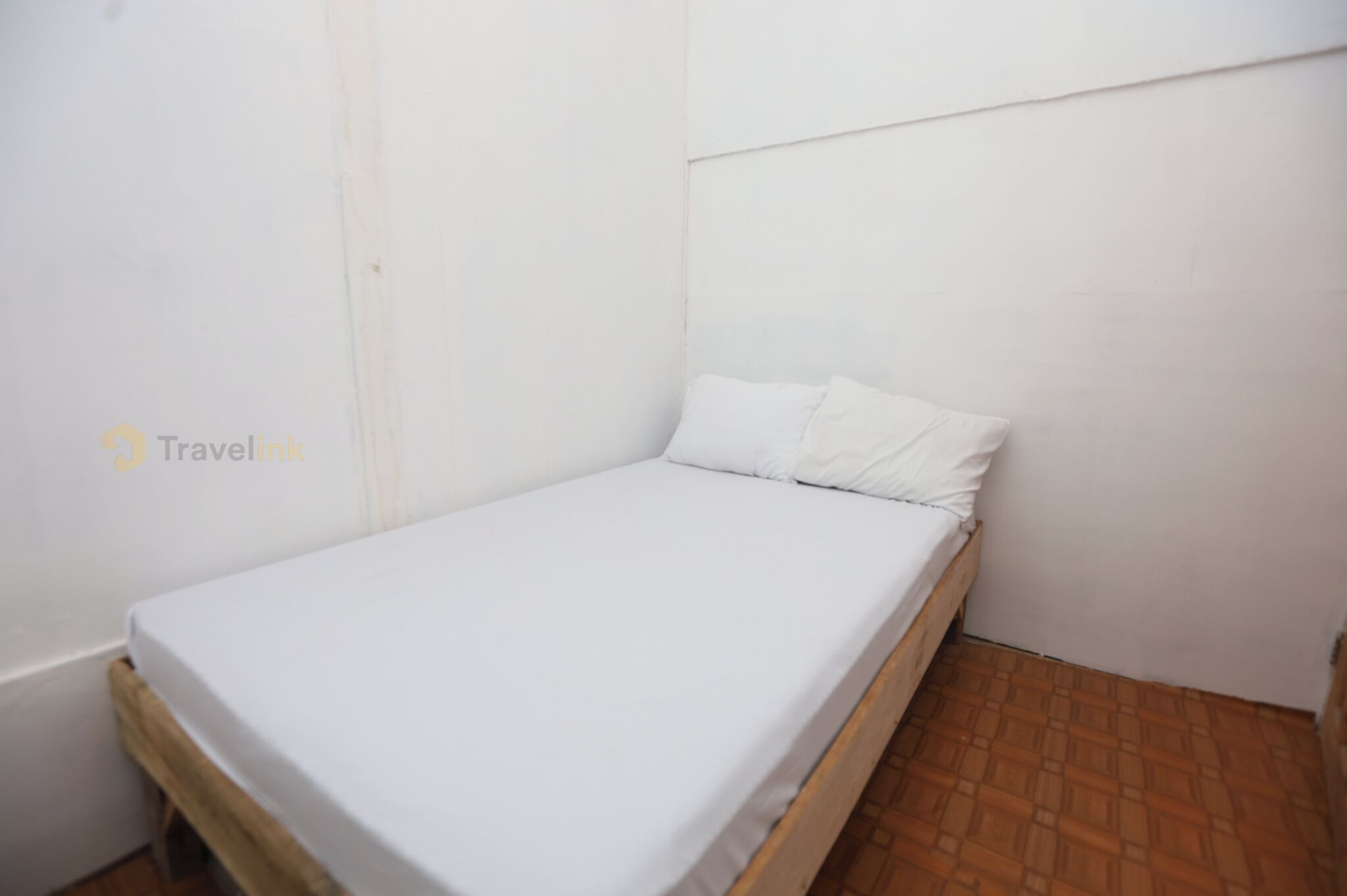 A small, single-bed room with a wooden frame, white bedding, and a tiled floor.