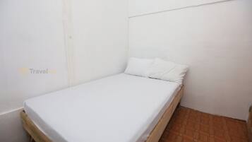 A small, single-bed room with a wooden frame, white bedding, and a tiled floor.