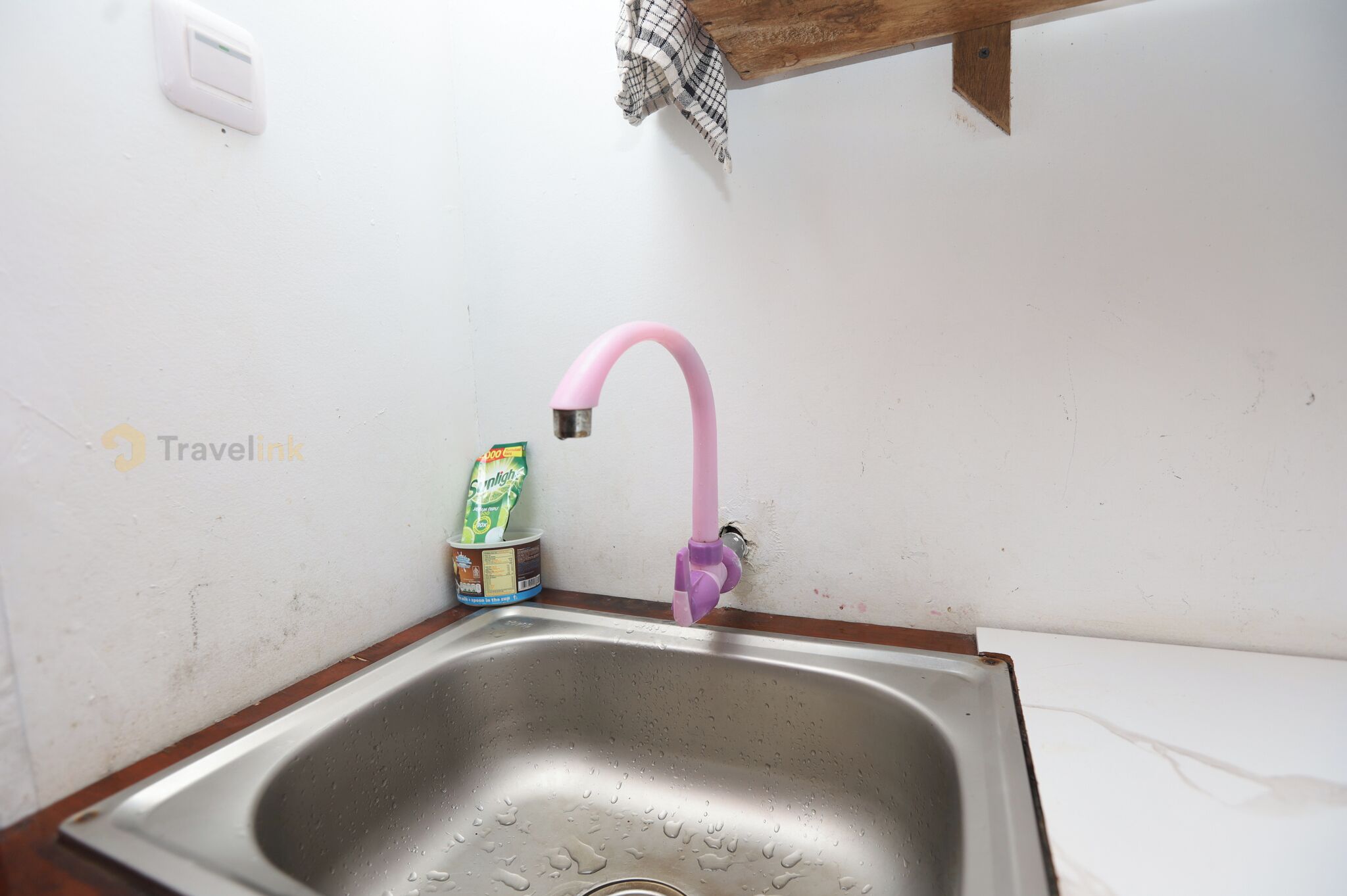 A kitchen sink with a pink faucet, a soap dispenser, and a small container of dish soap.