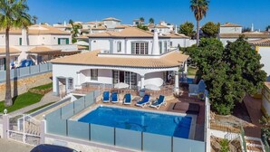Una casa grande con piscina, varios sillones de descanso y un patio cercado.