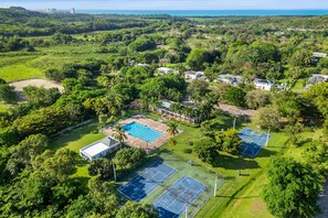 Vue aérienne d’un complexe hôtelier doté de plusieurs courts de tennis, d’une piscine et d’une végétation luxuriante.