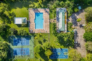 Vue aérienne d’une propriété dotée d’une piscine, de courts de tennis et d’un terrain de basketball, le tout entouré de verdure.