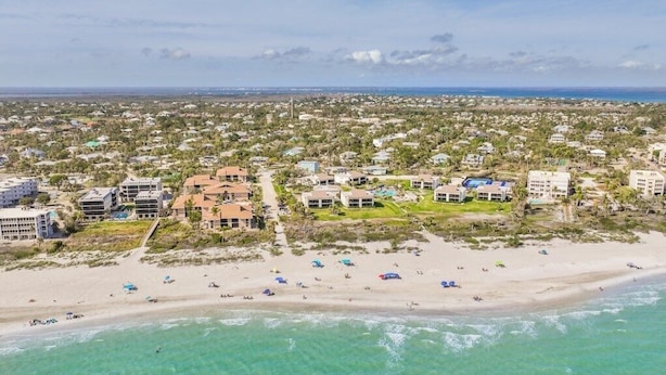 An aerial view of a coastal area with beachfront properties, including buildings with multiple stories and a sandy beach with umbrellas. - Shell Shack - New Luxurious Home (Sanibel)