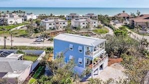 A coastal residential area with modern houses, a prominent blue building with a balcony, and a view of the ocean. - Shell Shack - New Luxurious Home (Sanibel)