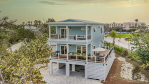 A multi-story beachfront property with a balcony, outdoor seating, and a view of the ocean. - Shell Shack - New Luxurious Home (Sanibel)