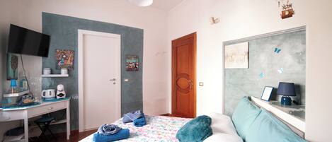 A bedroom with a bed, a desk, a chair, a television, and a hot air balloon decoration.