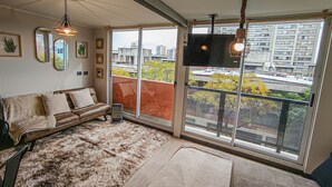 Ett mysigt vardagsrum med en brun lädersoffa, en mjuk matta och ett stort fönster med utsikt över staden.