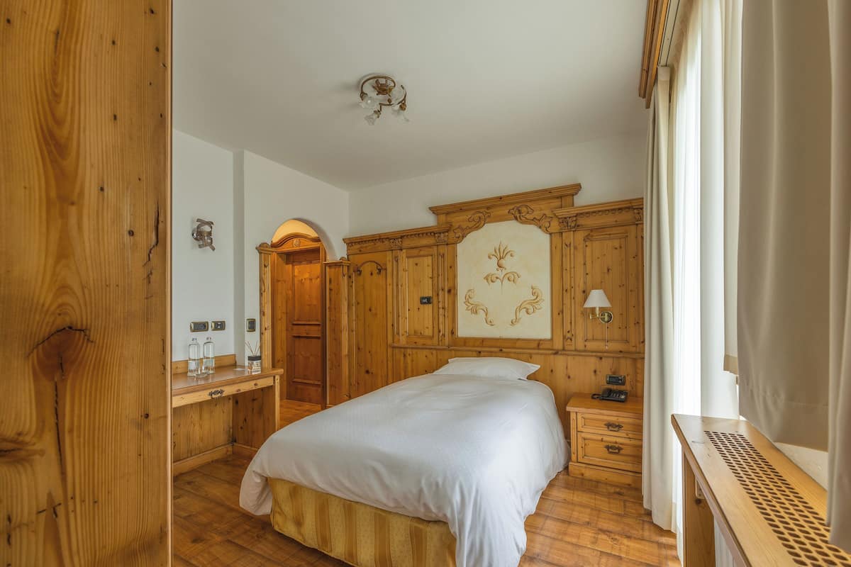 A wooden bedroom with a bed, a nightstand, a dresser, and a mirror.