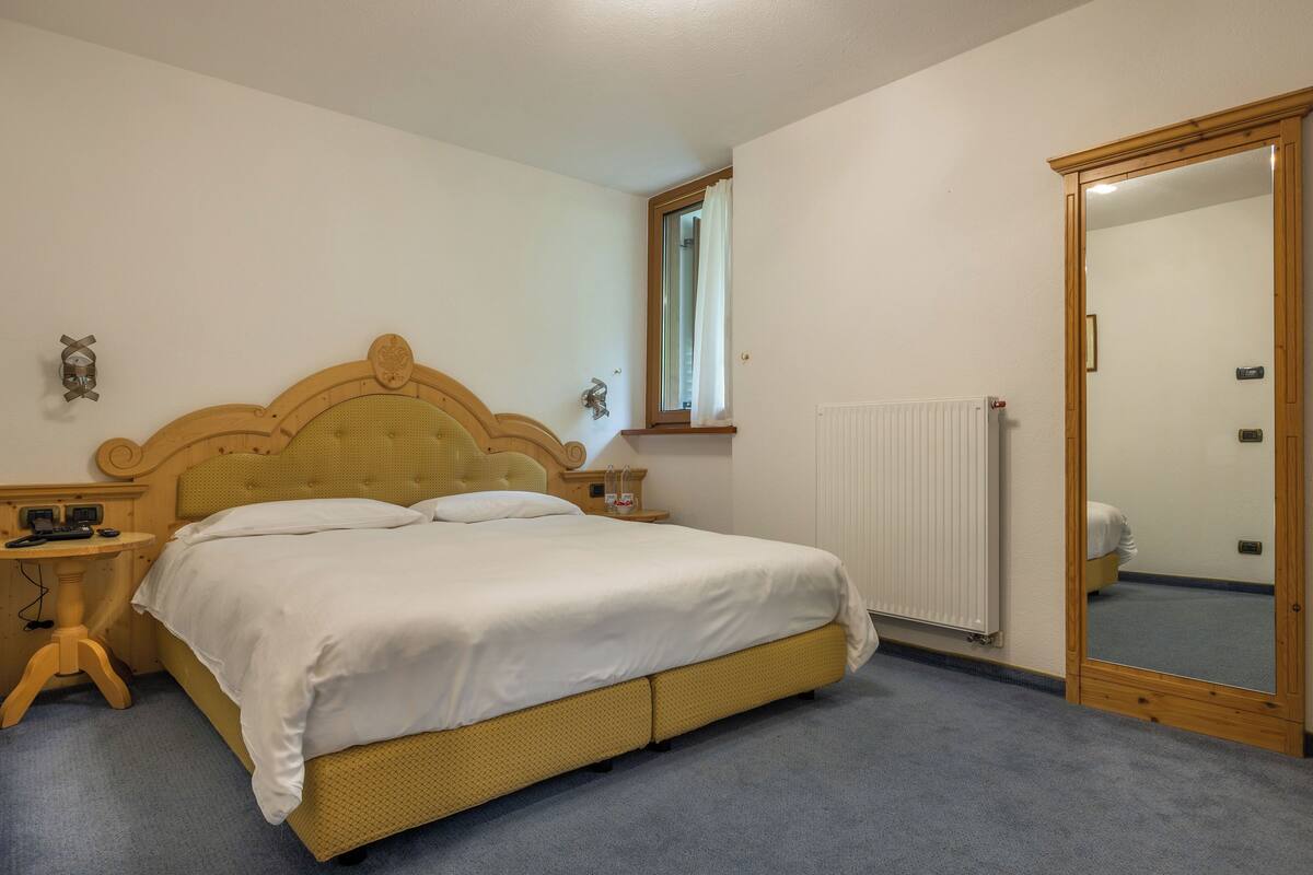 A bedroom with a wooden bed, a nightstand, a mirror, and a window with a curtain.