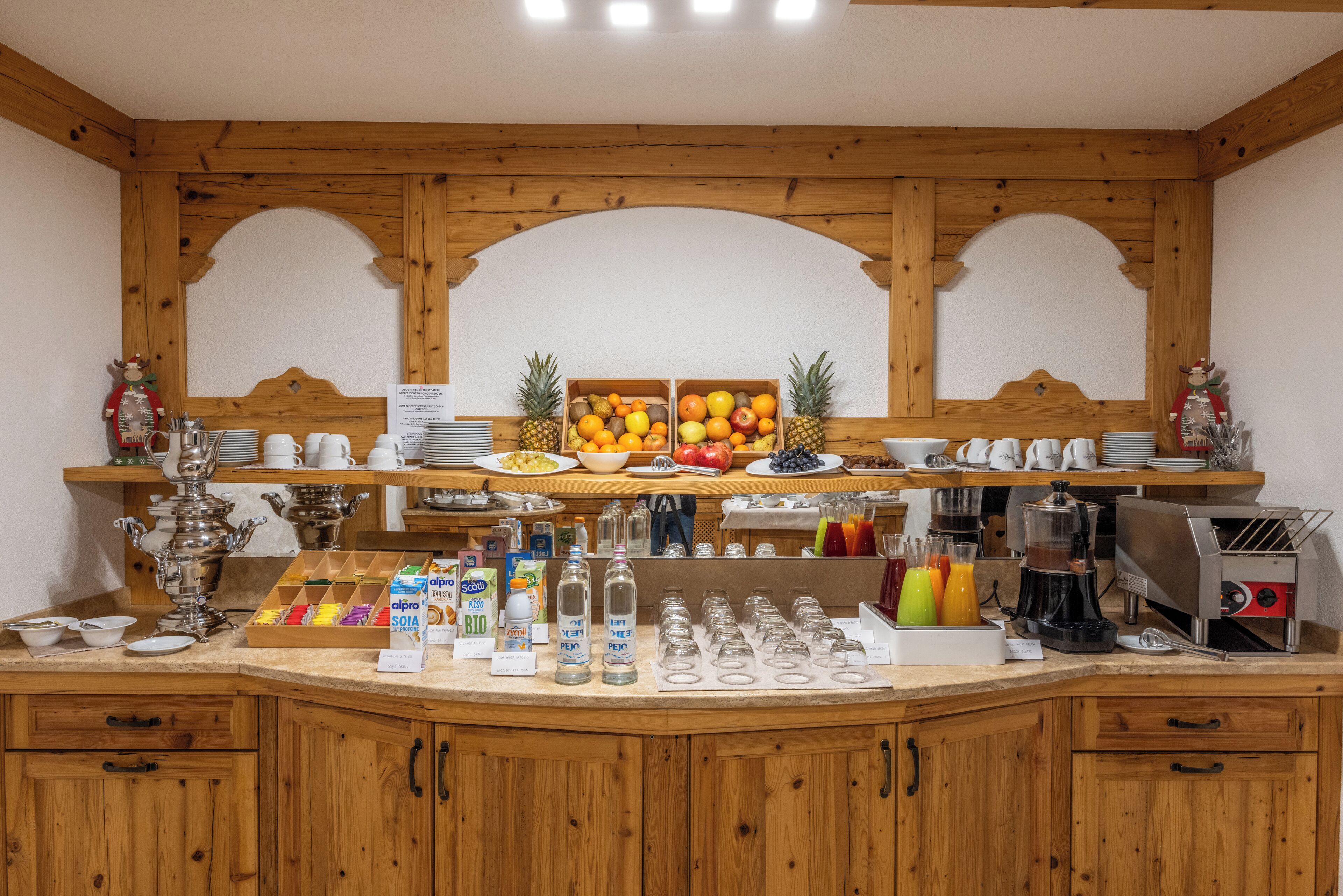 Una barra de desayuno con armarios de madera, una exhibición de frutas y diversas opciones para el desayuno, como jugos y café.