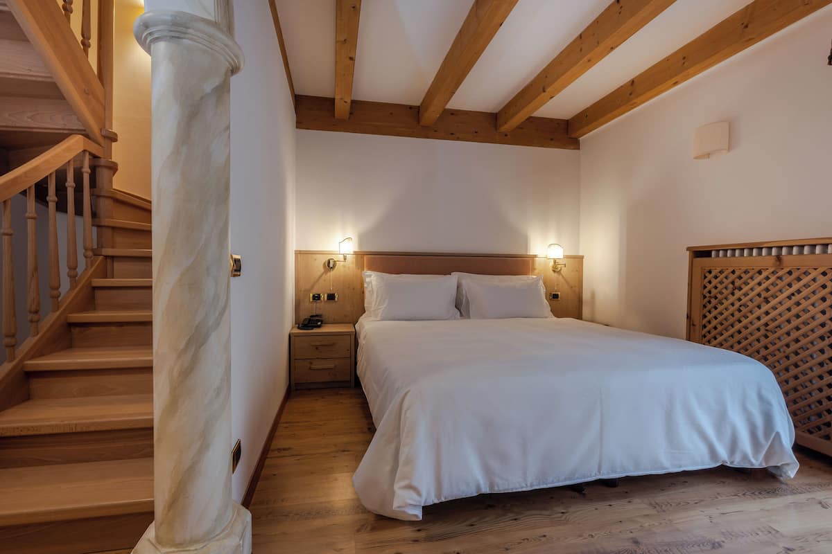 A bedroom with a wooden staircase, a bed with white bedding, and a nightstand with a lamp.