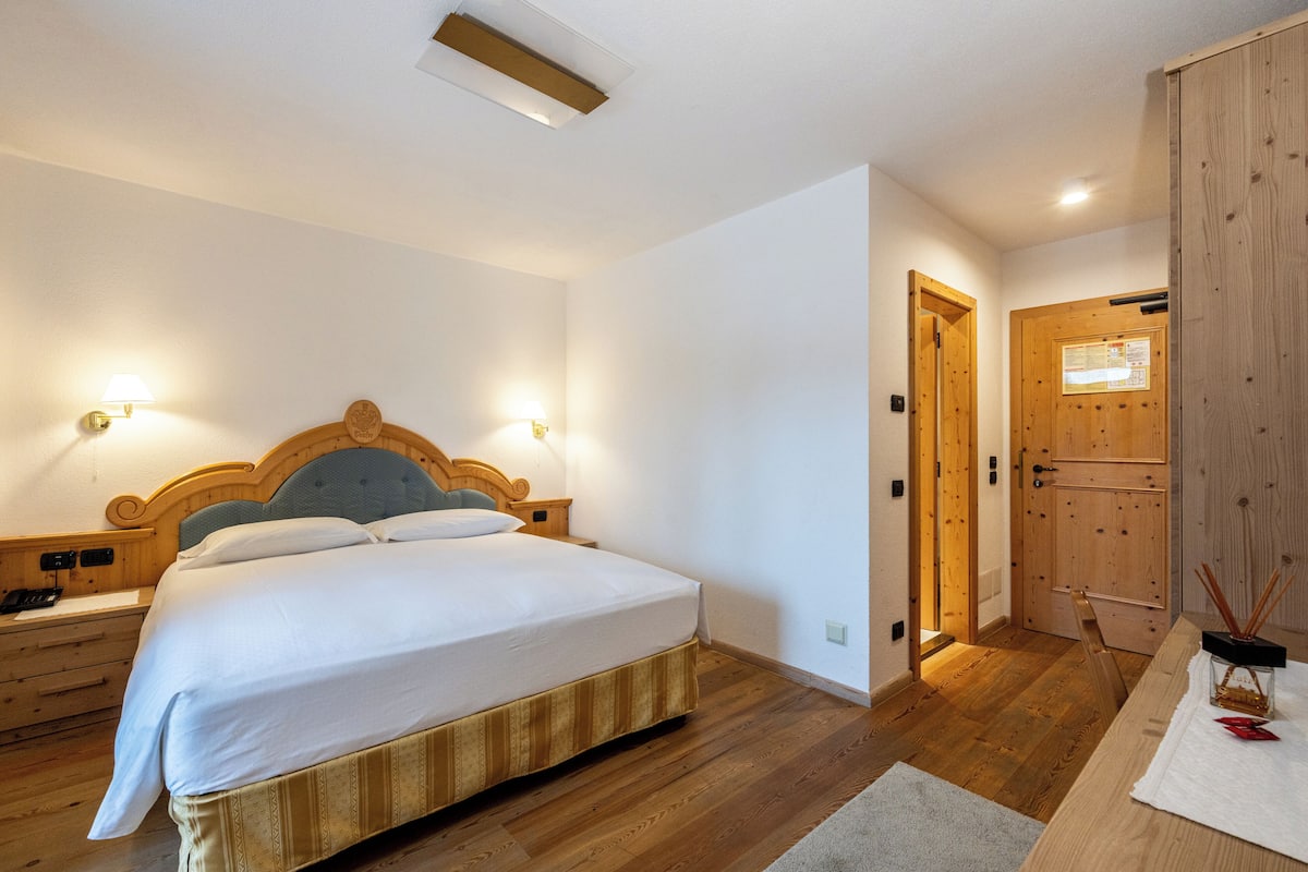 A bedroom with a wooden bed, nightstands, a wooden wardrobe, and a door with a bulletin board.