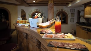 Un espace bar avec un comptoir en bois, un verre d’une boisson rouge et divers aliments, notamment des viandes et des fromages.