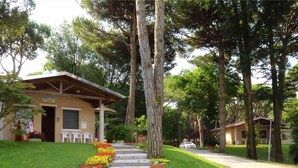 A building with a porch and a pathway leading to it, surrounded by trees and a well-maintained lawn. - Villaggio California Bungalow for 5 persons (Eraclea)