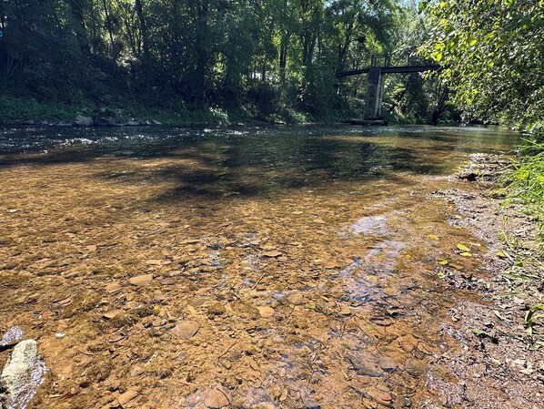 A clear river with visible rocks and a bridge in the background.