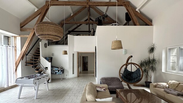 A spacious loft with high ceilings, exposed wooden beams, a foosball table, a sofa, a hanging chair, and a staircase leading to an upper level. - House to rent for summer holiday weekends for 8 -9-10- 11 - 12 - 13 persons (Compolibat)