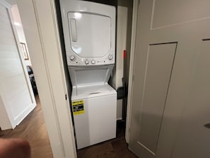 A compact, white, front-loading washer and dryer unit with an ENERGY GUIDE sticker, located in a narrow hallway with wooden flooring and white walls. - Quaint Lodge 1.5 miles Dollywood, Quaint Lodge 1.5 m to Dollywood (Sevier County)
