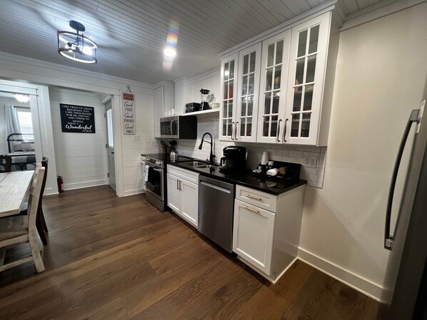 A kitchen with white cabinets, a black countertop, stainless steel appliances, and a wooden floor.