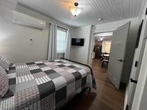 A bedroom with a bed, a television, and a door leading to a kitchen.