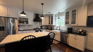 A modern kitchen with white cabinets, stainless steel appliances, and black pendant lighting.