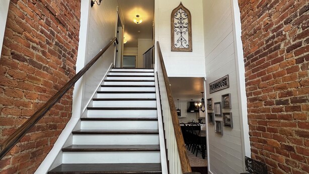 A staircase with wooden steps and white walls, leading to a dining area with a chandelier and framed pictures.