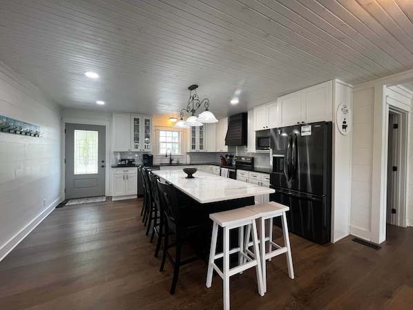 A modern kitchen with white cabinetry, a central island with stools, a black refrigerator, and a microwave.
