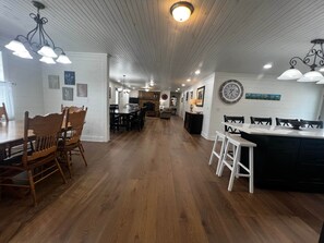 A spacious kitchen with wooden flooring, a dining area with wooden chairs, and a kitchen island with a black countertop.