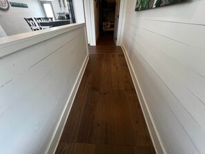 A hallway with a wooden floor and white walls, leading to a kitchen area.
