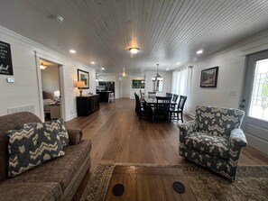 A spacious living room with a dining area, wooden floors, and a kitchen in the background.