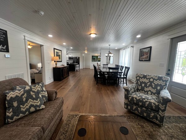 A spacious living room with a dining area, wooden floors, and a kitchen in the background.