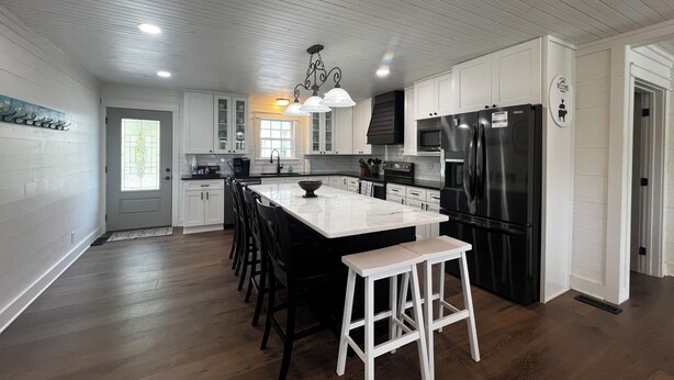 Una cocina moderna con armarios blancos, un refrigerador negro y una isla grande con taburetes.